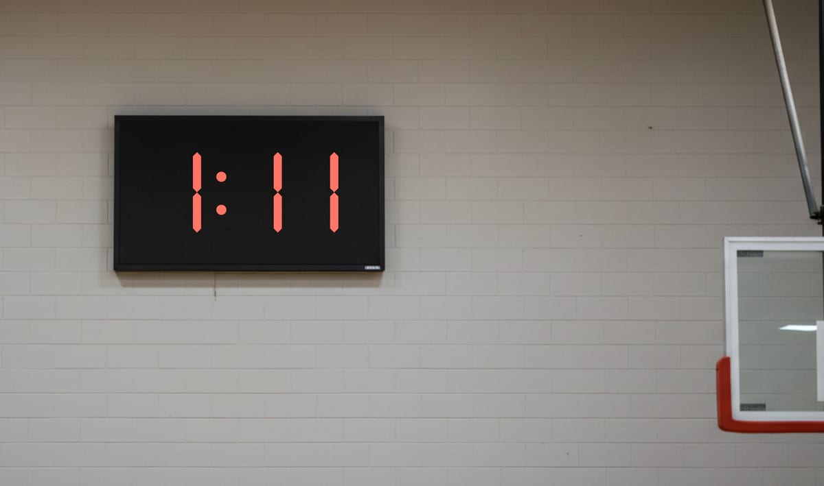 A red LED wall clock in a school gym reading 1:11.